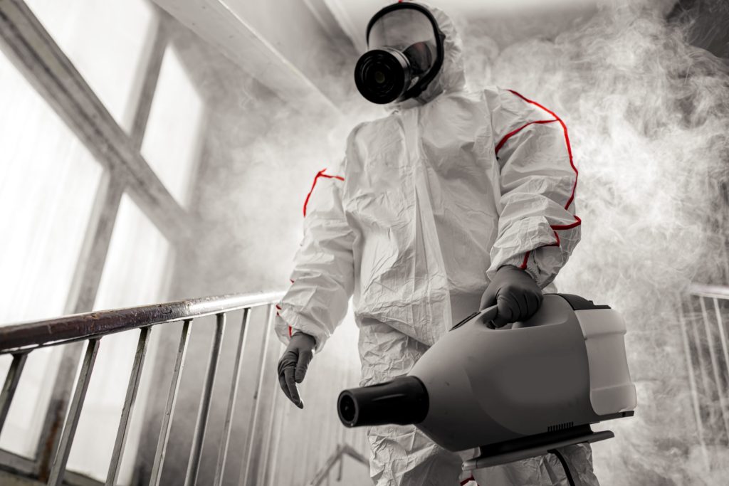 Person in hazmat suit with fogging sprayer