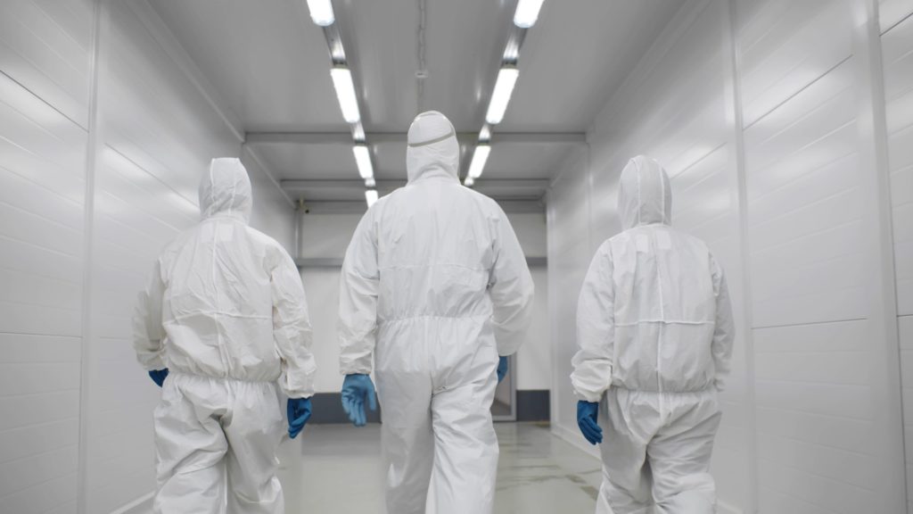 Three people in hazmat suits walking down corridor