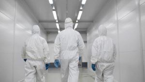 Three people in hazmat suits walking down corridor